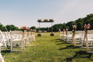 Wedding altar made of wooden sticks and bouquets stands before the rows of white garden chairs
